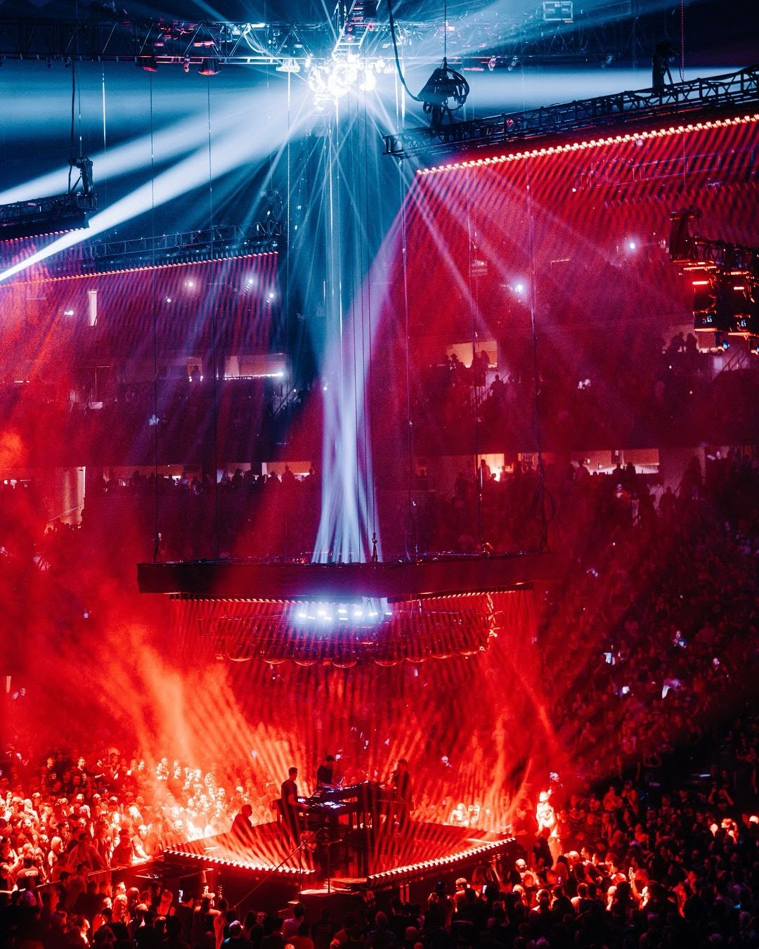 trent reznor, atticus ross and boys noize stood on a square stage surrounded by an audience and red and blue light