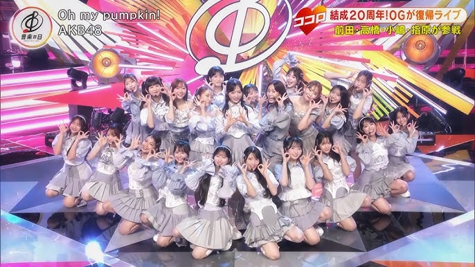 members Akiyama Yuna, Arai Sae, Oguri Yui, Kuranoo Narumi, Sato Airi, Chiba Erii, Mukaichi Mion, Yagi Azuki, Yamauchi Mizuki, Ito Momoka, Hanada Mei, Shania Gracia, Hoop, CJ, Gui ChuChu, Lin Yu-hsin, Lookked, Yi Shyan, Kojima Haruna, Sashihara Rino, Takahashi Minami and Maeda Atsuko standing on stage in a triange formation