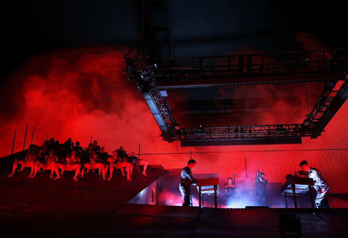 photo of the stage showing multiple people huddling like insects at the top of a metal slope with Atticus Ross, Mariqueen Maandig Reznor, Trent Reznor and Boys Noize stood in an carved out indent to the right of them. The whole photo is lit with red and light and a lot of fog