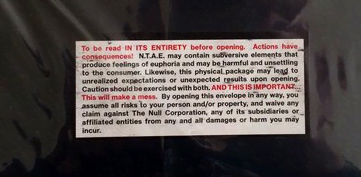 a non descript black plastic wrapped parcel with a small warning label reading: To be read IN ITS ENTIRETY before opening. Actions have consequences! N.T.A.E. may contain subversive elements that produce feelings of euphoria and may be harmful and unsettling to the consumer. Likewise, this physical package may lead to unrealized expectations or unexpected results upon opening. Caution should be exercised with both. AND THIS IS IMPORTANT... This will make a mess. By opening this envelope in any way, you assume all risks to your person and/or property, and waive any claim against The Null Corporation, any of its subsidiaries or affiliated entities from any and all damages or harm you may incur.