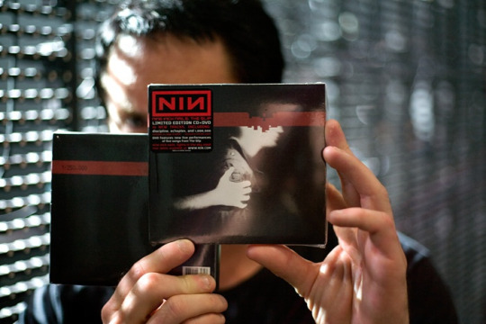 Trent Reznor holding up two copies of the slip CD, obscuring his face.