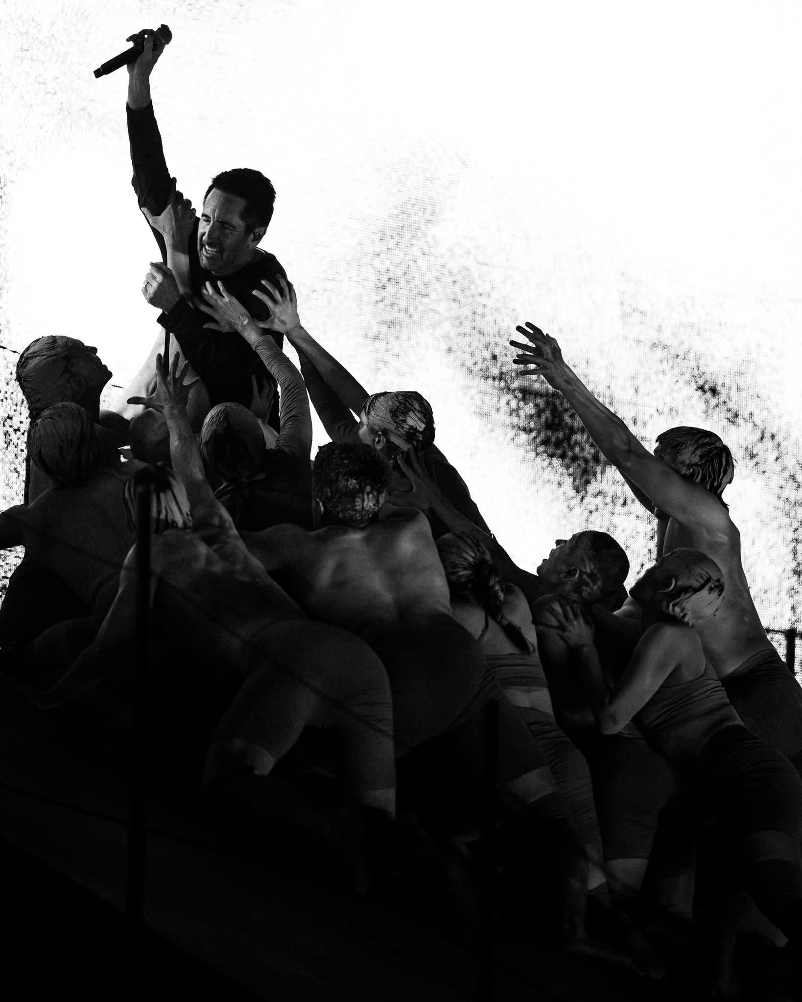 black and white image showing trent reznor reaching up out of a pile of people dragging him down
