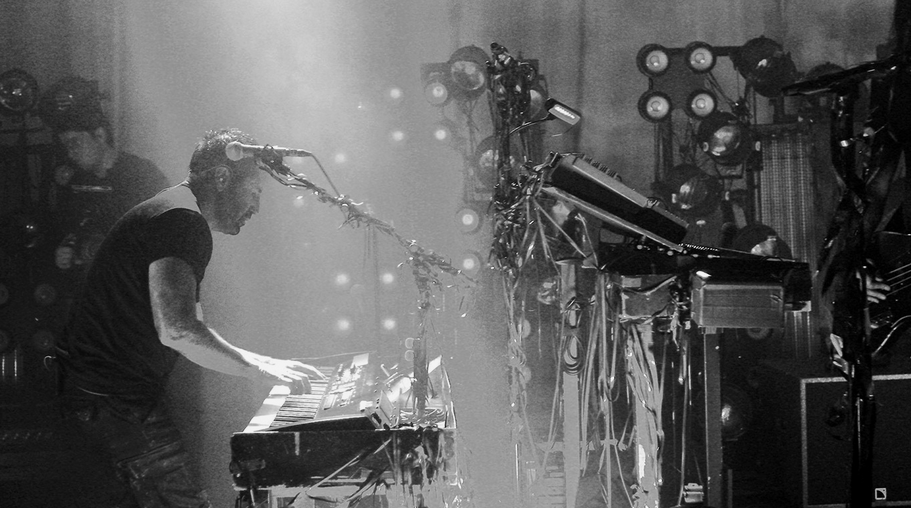 black and white photo of trent hunched over a his keyboard, the synths opposite are tangled in tape 